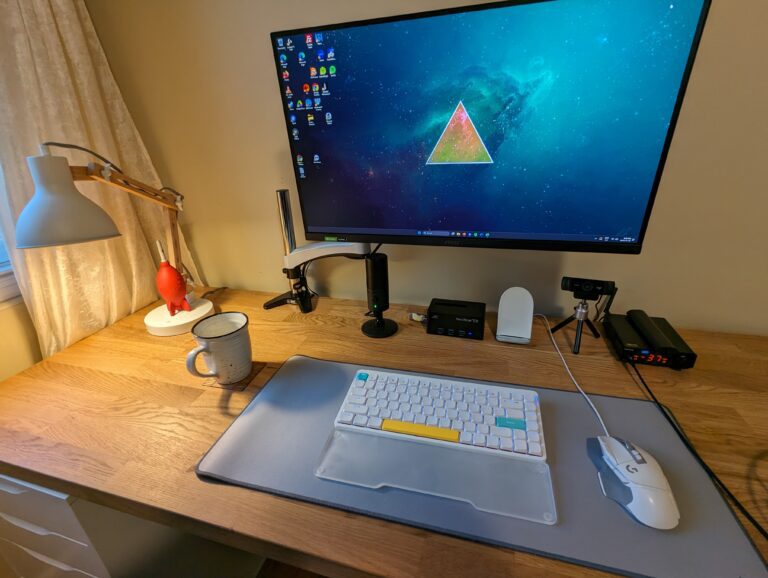 Gaming Computer with custom mechanical keyboard, desk mat, logitech mouse, and a 27" monitor mounted on an arm.
