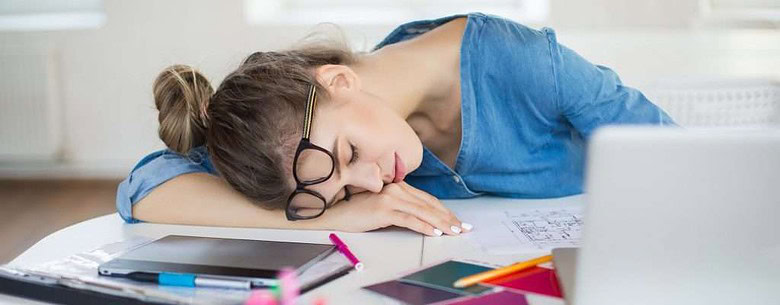 Young tired woman with eyeglasses on head sleeping on desk due to fatigue