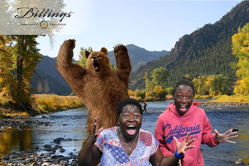 Denver greenscreen photo booth at the 2022 Travel and Adventure Show featuring Visit Billings. Two participants "run" from a bear as he rears up on a scenic river.