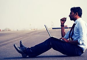 Man sitting on a road with a laptop contemplating his future