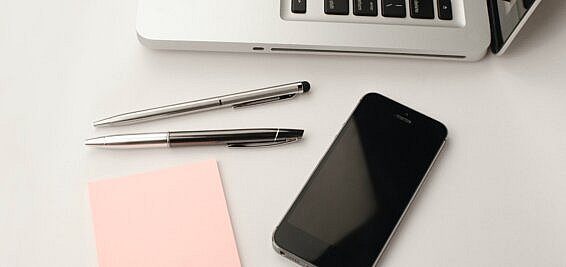 laptop, post-it pad, pens and iphone on a desk