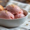 Homemade-Caramelised-Plum-And-Cardamom-Ice-Cream-featured-image Bowl of homemade caramelised plum and cardamom ice cream topped with seeds with fresh plums on a wooden table Frosted Fusions