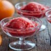Learn-How-To-Make-The-Perfect-Blood-Orange-Sorbet-featured-blood-orange Sorbets in glass dishes with fresh blood orange to the side-Frosted-Fusions