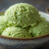Homemade-Matcha-Ice-Cream-Recipe-–-A-Taste-Of-Japan-featured-image-bowl-of-matcha-ice-cream-with-matcha-powder-in-bowls-in-background-and-green-tea-leaves-Frosted-Fusions
