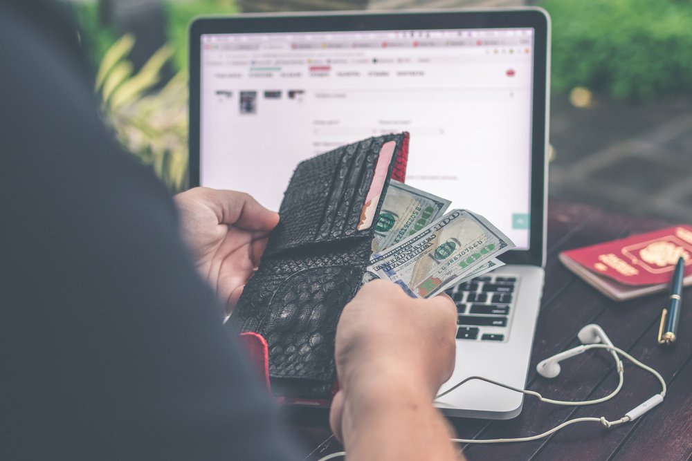 A photo of someone handling money in their wallet in front of a laptop