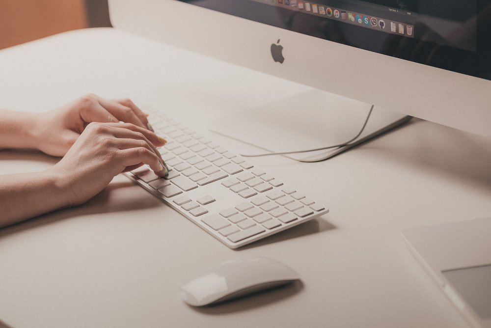 A photo of a woman's hands on a Mac keyboard about to write a business propsal