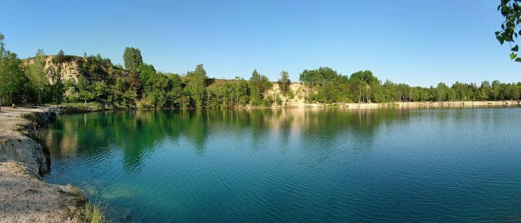 A calm lake with clear blue water, surrounded by trees and a rocky shoreline under a sunny sky, offers a tranquil escape reminiscent of hidden Krakow beaches.