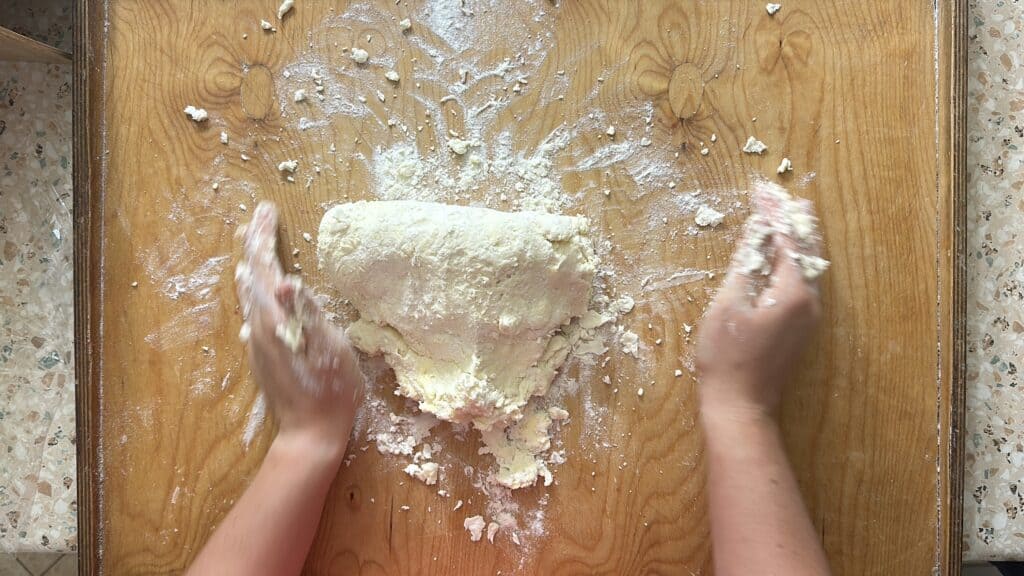 Hands kneading dough on a floured wooden surface, preparing an easy kolacky recipe.