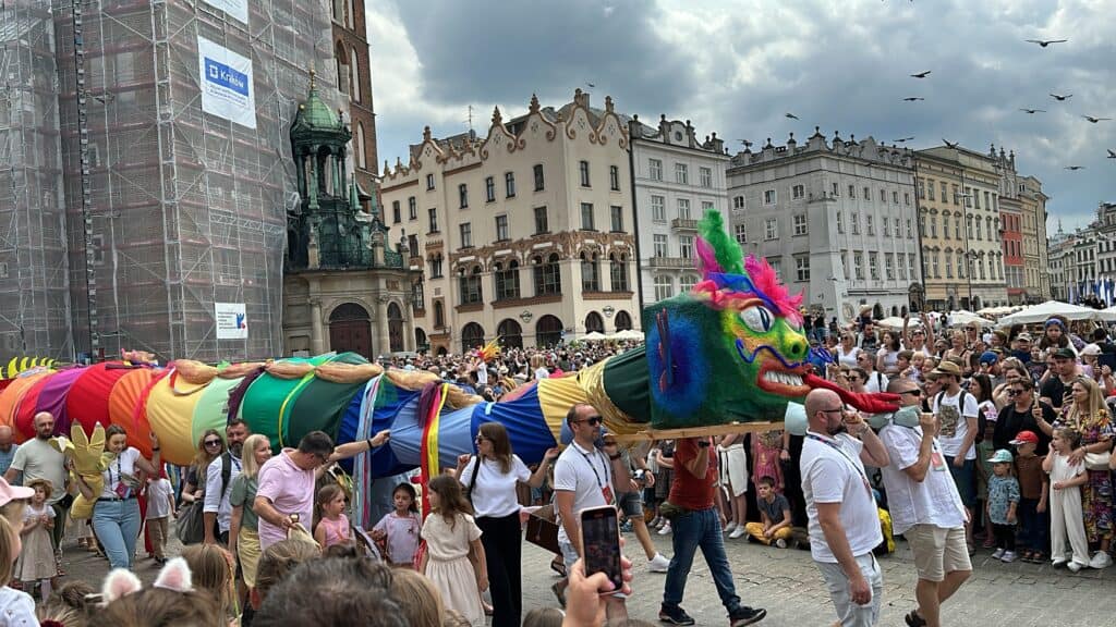 A colorful dragon puppet is carried by a group of people in a crowded city square during a public event or parade&mdash;a must-see for first time visitors seeking authentic Krakow travel experiences.