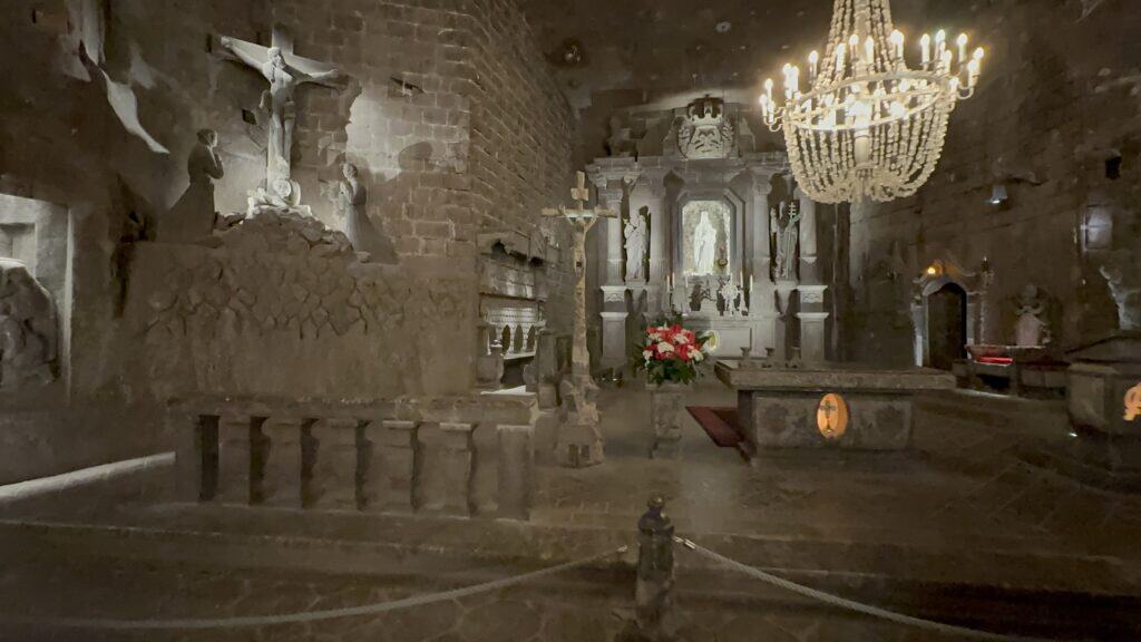 Dimly lit stone chapel interior with religious statues, an altar adorned with flowers, and a chandelier hanging from the ceiling&mdash;one of the beautiful places in Poland worth visiting.