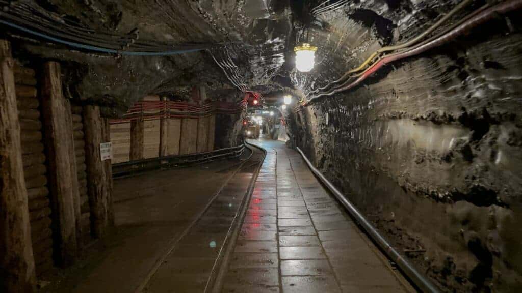 Underground mining tunnel with dim lighting, exposed cables, and tracks running along the tiled floor&mdash;perfect for those seeking unique travel experiences or looking for visiting tips to explore Bochnia Salt Mine.