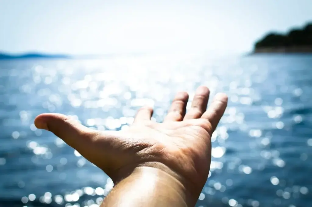 Sun-kissed hand reaching towards a sparkling ocean, inviting connection with natures tranquility.