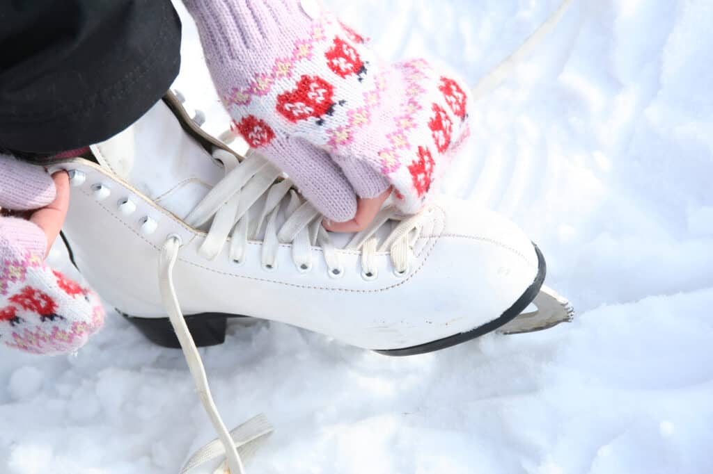 In Krak&oacute;w this December, a person wearing pink patterned gloves ties the laces of a white ice skate on snow&mdash;one of the charming things to do in winter.
