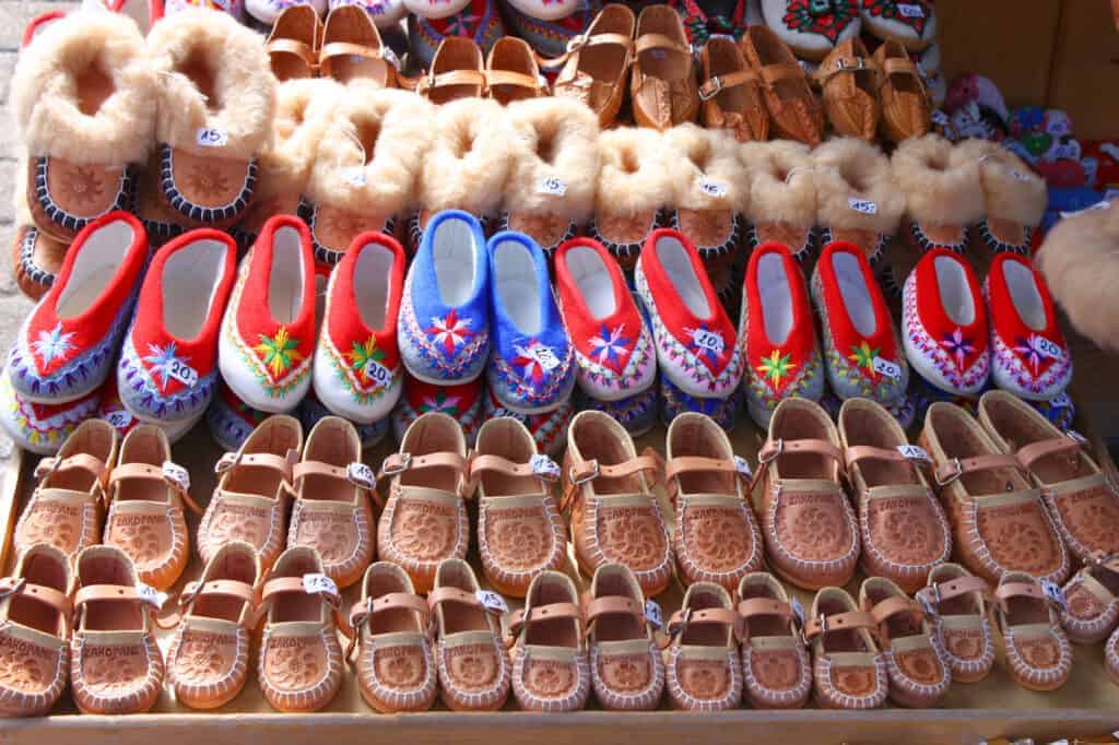Rows of traditional handmade slippers and shoes, some with fur trim and others with colorful embroidery, displayed for sale at a market stall&mdash;perfect Polish souvenirs and unique things to buy in Poland.