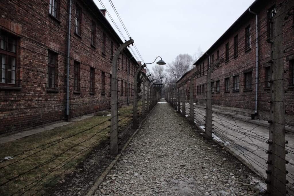 Barbed wire fences separate two rows of brick buildings along a gravel path under a cloudy sky&mdash;one of the historic sites often included in the best day trips from Krakow.