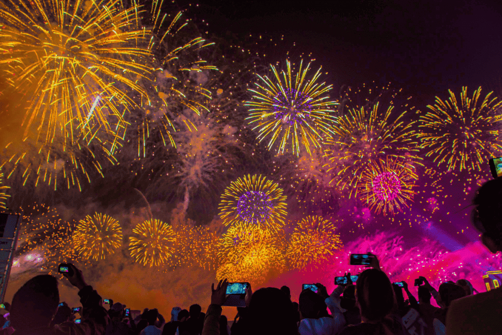 Crowd of people taking photos of colorful fireworks lighting up the night sky, capturing the magic of Polish New Year's traditions at a festive outdoor celebration.