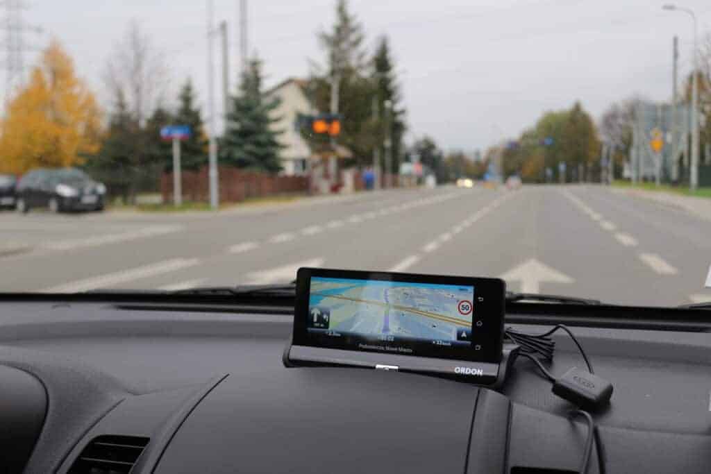 A GPS device displaying navigation instructions&mdash;using one of the top Poland travel apps&mdash;is mounted on the dashboard of a car driving down a mostly empty street.