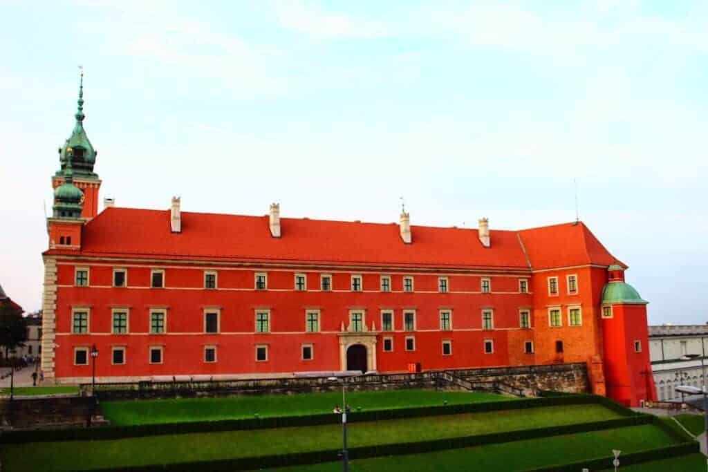 A large red brick building with a tall clock tower, green lawn in front, and a clear sky in the background&mdash;this striking landmark is a highlight of Poland tourism and ranks among the must-see castles in Poland.