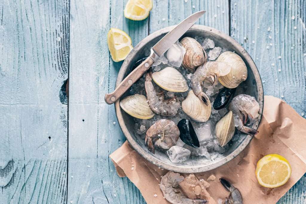 Bowl of clams on ice with lemons as an example of iron intake through seafood. Baseline diet is an important consideration before supplementing with iron IV therapy.