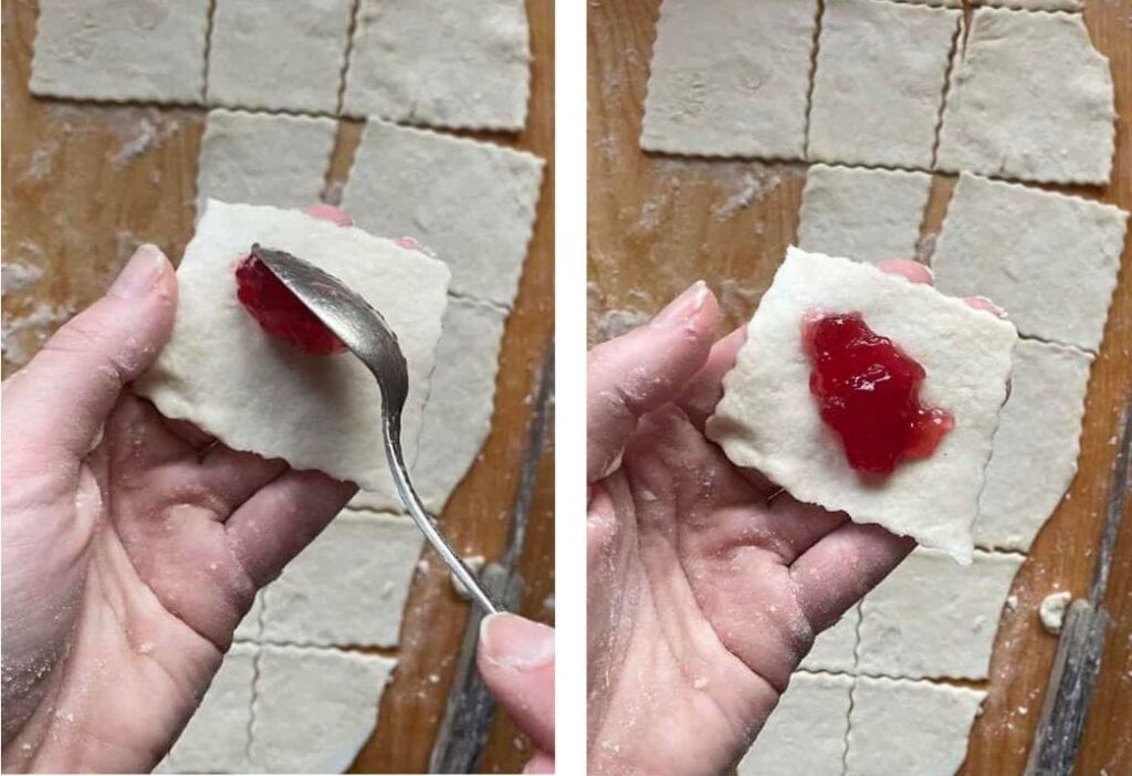Hands meticulously folding pastry dough squares, spreading vibrant red jam on one. More Smalc&oacute;wki squares rest in the background on a rustic wooden surface, capturing the essence of traditional Polish cookies.