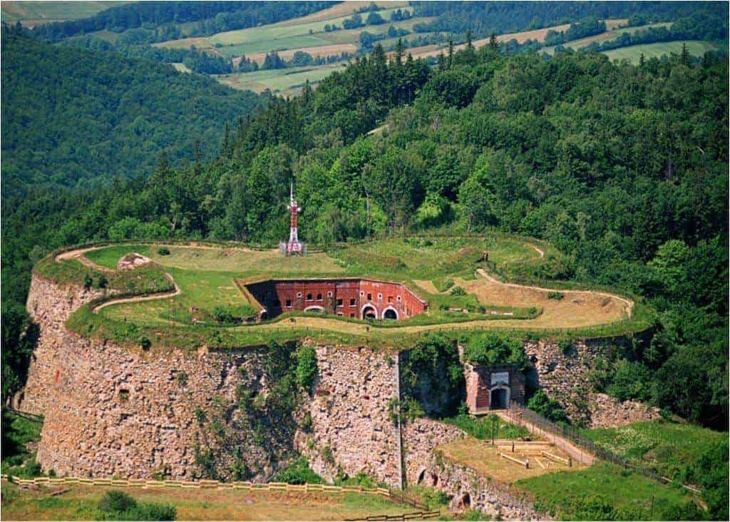 Aerial view of a star-shaped stone fortress surrounded by greenery and trees, with rolling hills in the background&mdash;a must-see in Dolnośląskie and one of the best places to visit in Poland.