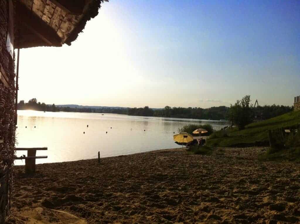 Sandy beach by a calm lake at sunset, with a wooden structure on the left, benches, and yellow umbrellas near the water&mdash;one of the relaxing beaches in Krakow perfect for unwinding.