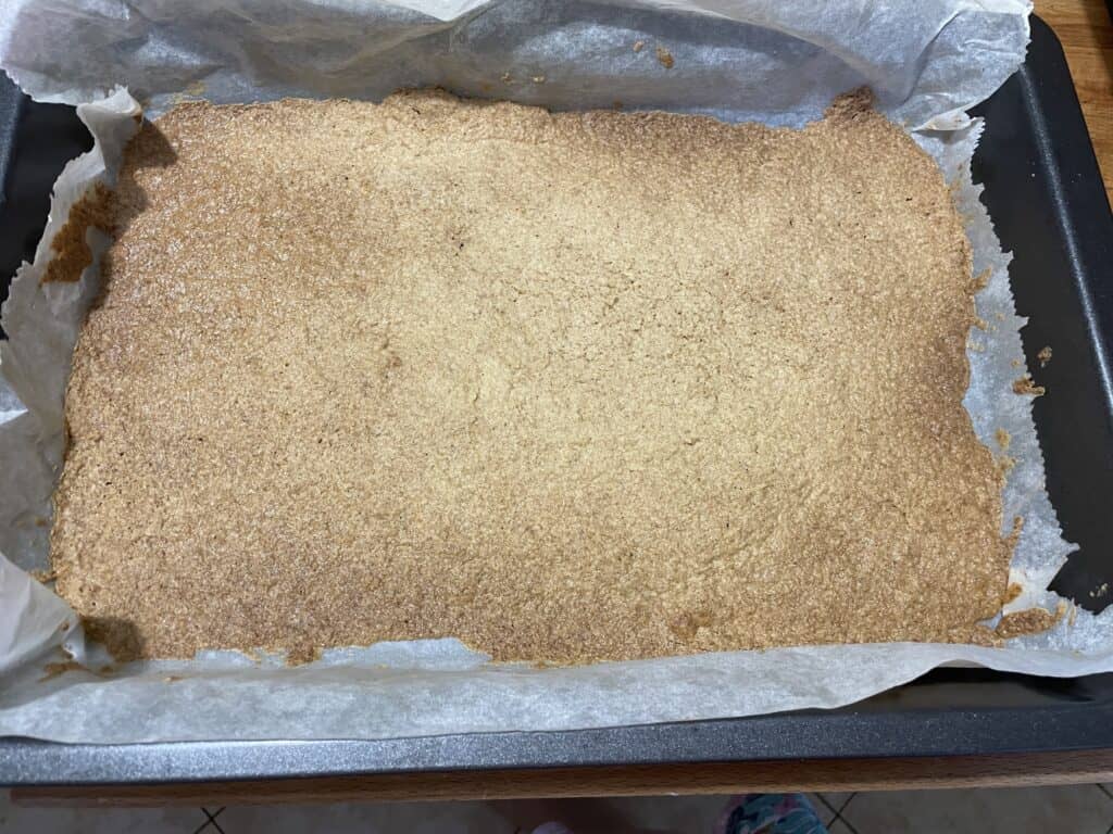 A freshly baked rectangular Polish vegan cheesecake on parchment paper, with a golden-brown, crumbly surface.