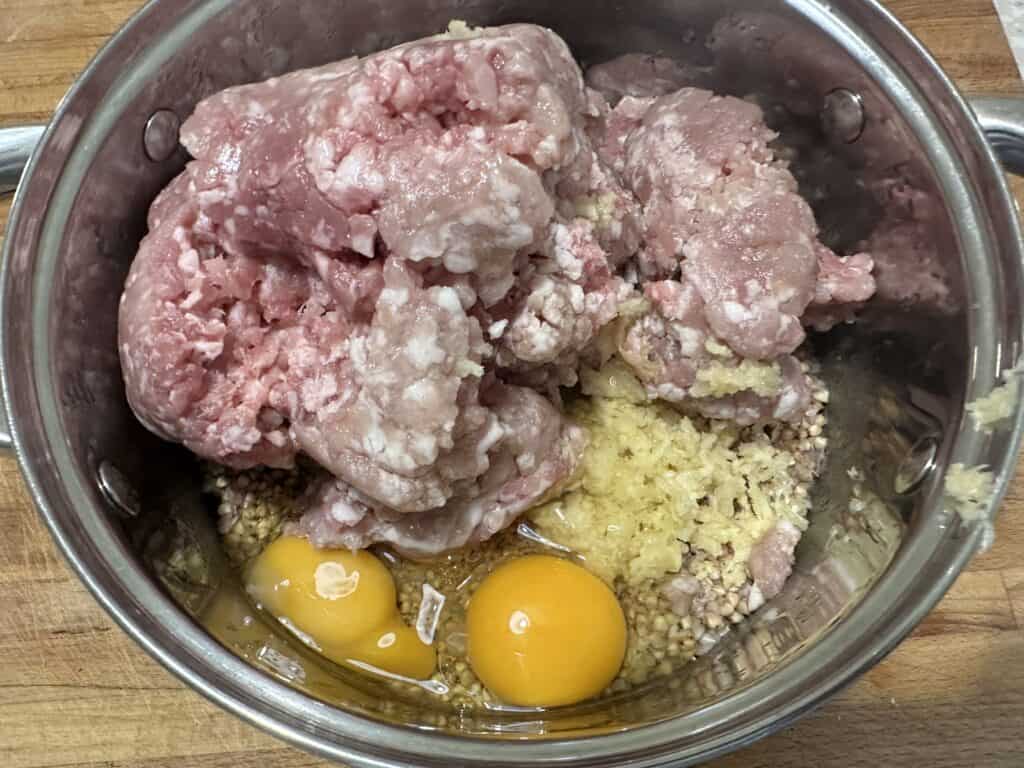 Ground meat, two raw eggs, and minced garlic blend together in a metal pot to create the perfect base for Polish Patties.