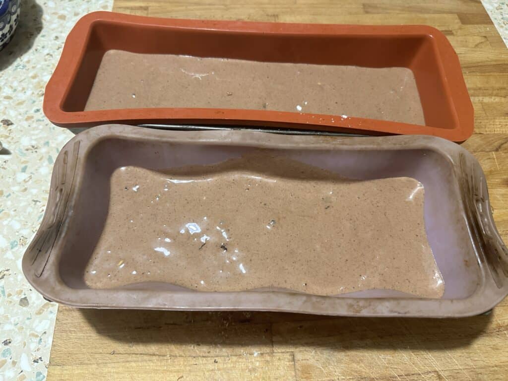Two silicone loaf pans filled with raw gingerbread cake batter sit on a wooden countertop, ready for a quick recipe delight.