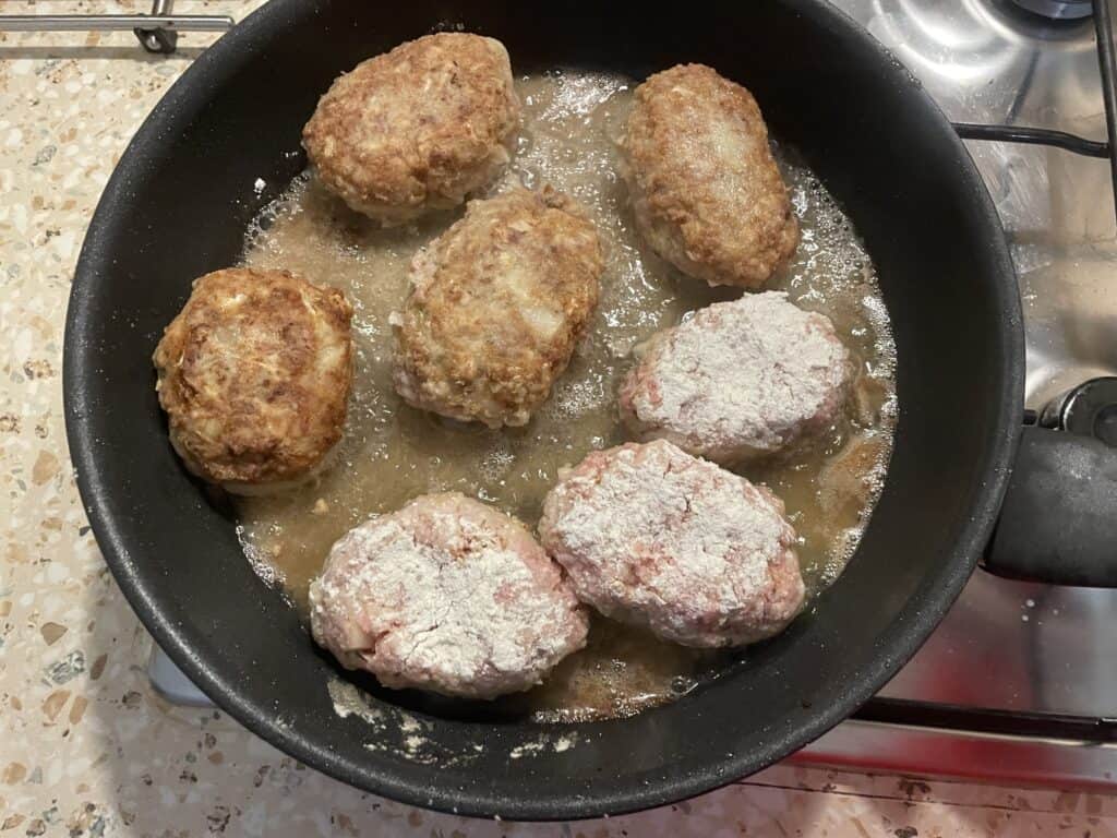 Seven breaded meat patties sizzle in a pan on the stovetop with a splash of oil, creating a quick recipe reminiscent of Gołąbki casserole.