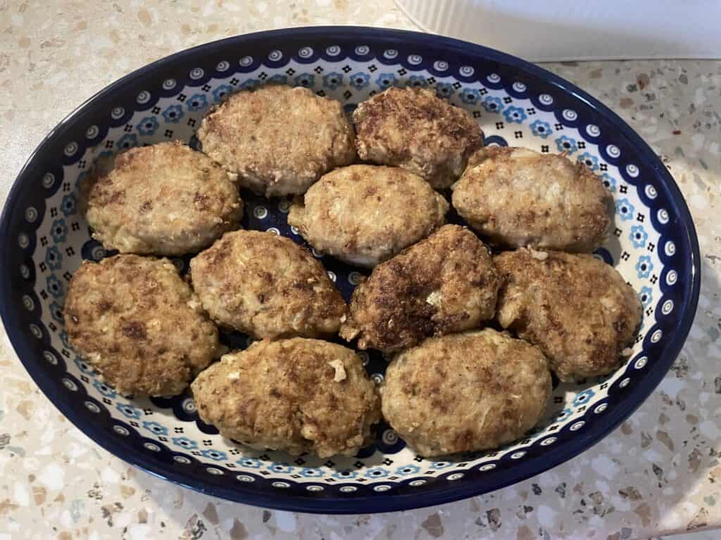 A decorative oval dish features ten browned, oval-shaped meat patties on a patterned surface, reminiscent of an unstuffed cabbage rolls recipe.