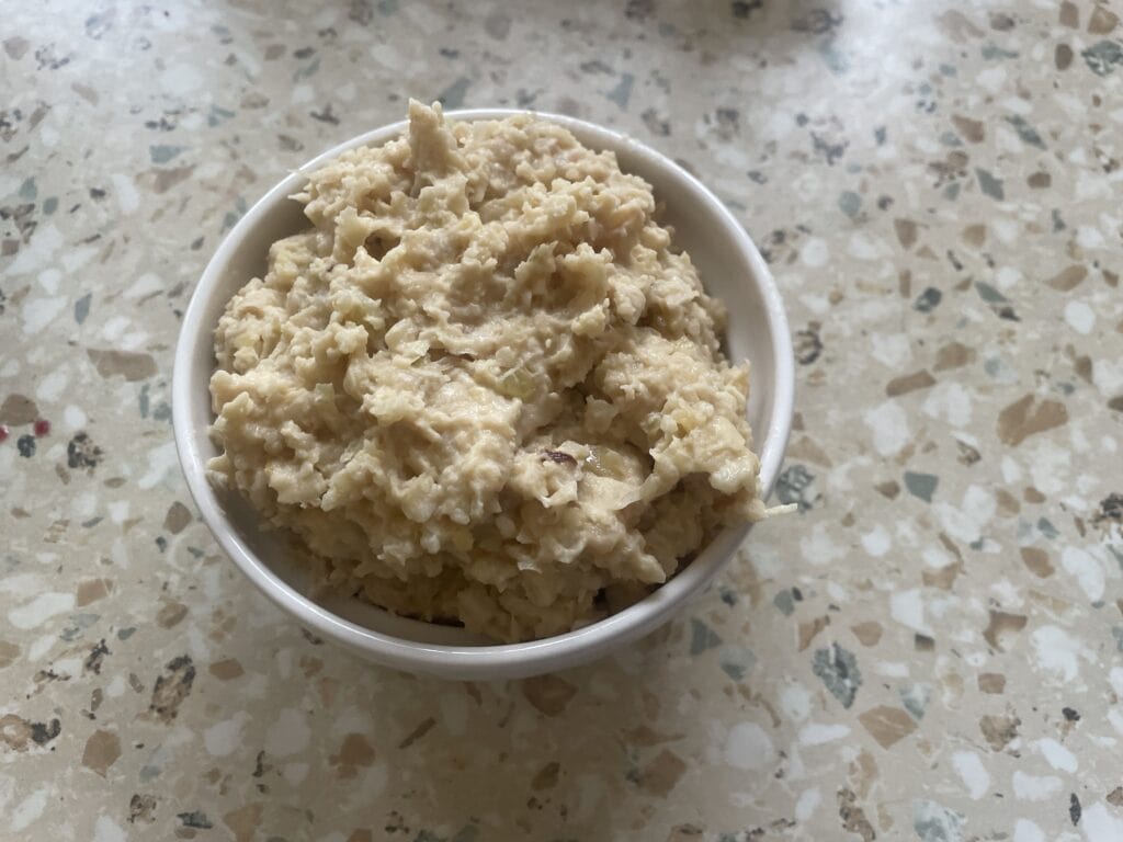A bowl of oatmeal with banana pieces on a speckled countertop sits next to a jar of Smalec Wegański, adding a Polish twist to your vegan breakfast.
