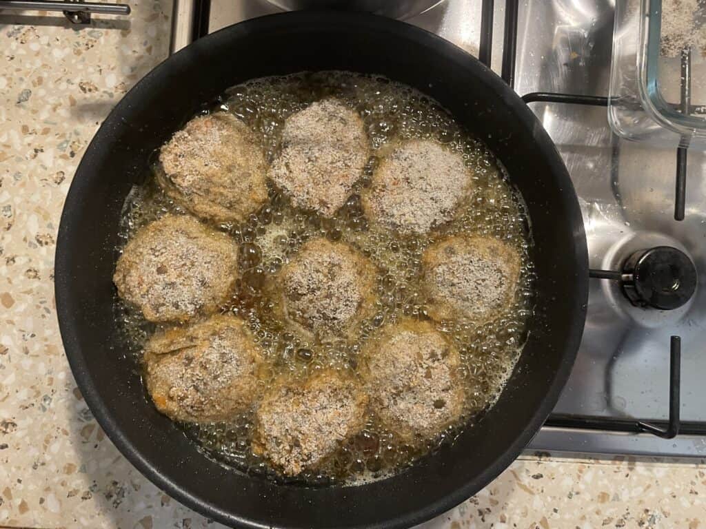 Eight golden cutlets sizzling in oil in a black pan on a stovetop, these delicious bites resemble classic Vegan Kotlety Mielone made from wholesome lentils.