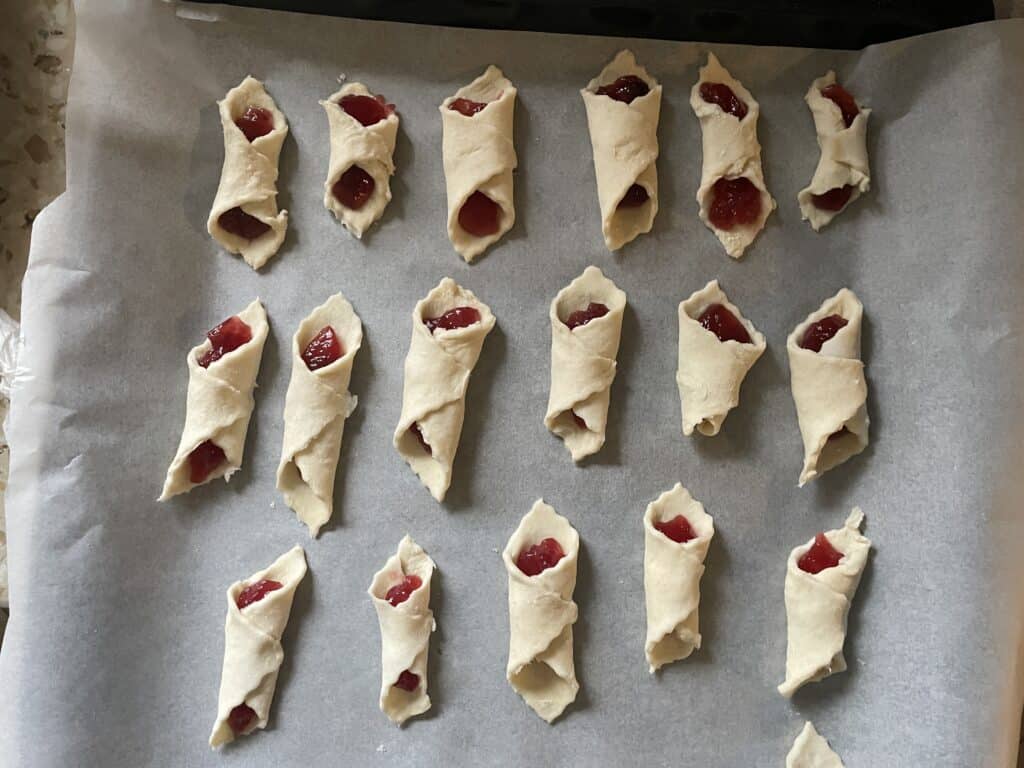 Unbaked Polish lard cookies filled with red jam sit poised on a parchment-lined baking sheet, ready for baking.