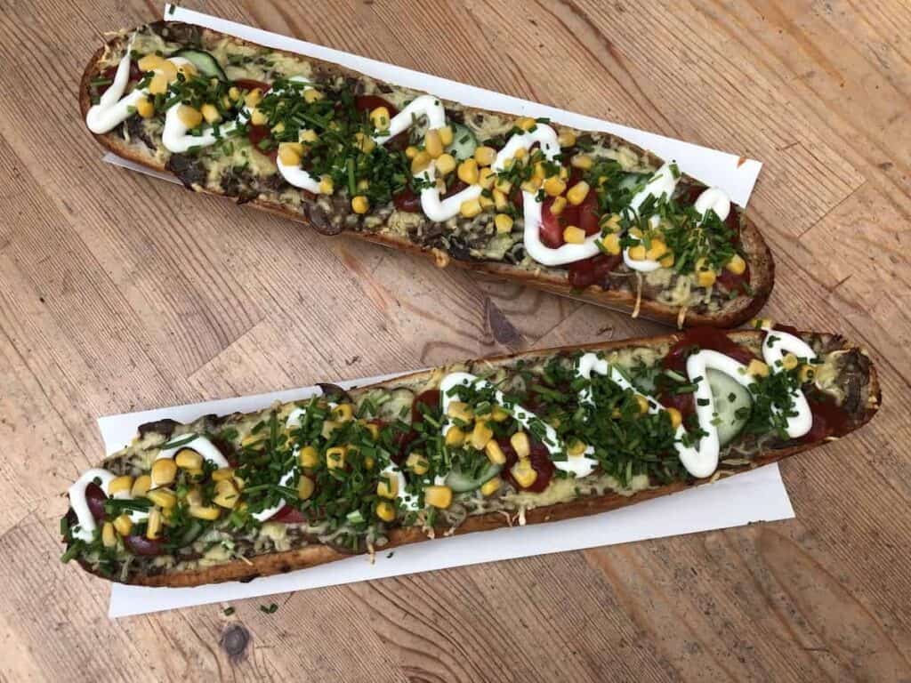 Two long open-faced sandwiches topped with sliced cucumbers, corn, shredded cheese, chopped herbs, ketchup, and mayonnaise&mdash;a delicious option if you&rsquo;re wondering where to eat in Krakow or exploring local Krakow restaurants.