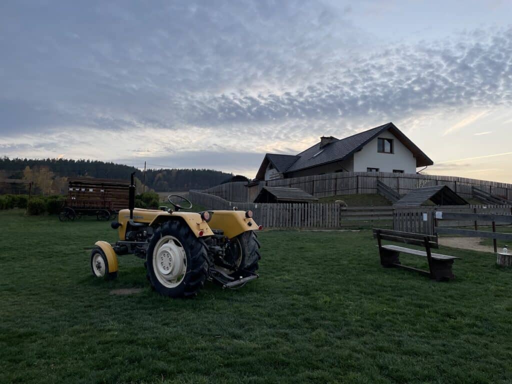 A yellow tractor is parked on a grassy lawn near a wooden bench, with a house and distant trees in the background at dusk&mdash;capturing the peaceful charm of autumn in Poland.
