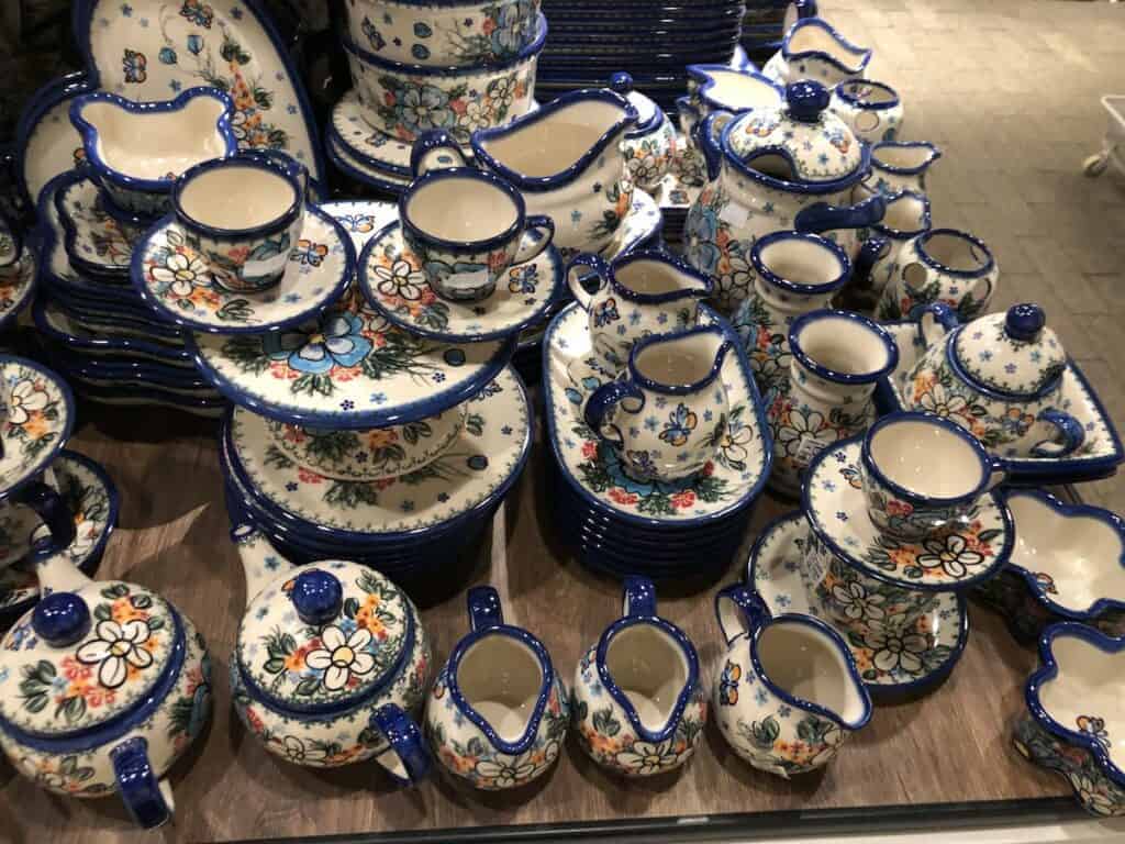 A display of colorful, floral-patterned ceramic dishware&mdash;including cups, saucers, pitchers, and plates&mdash;arranged on a wooden surface showcases popular Poland souvenirs and charming things to buy in Poland.