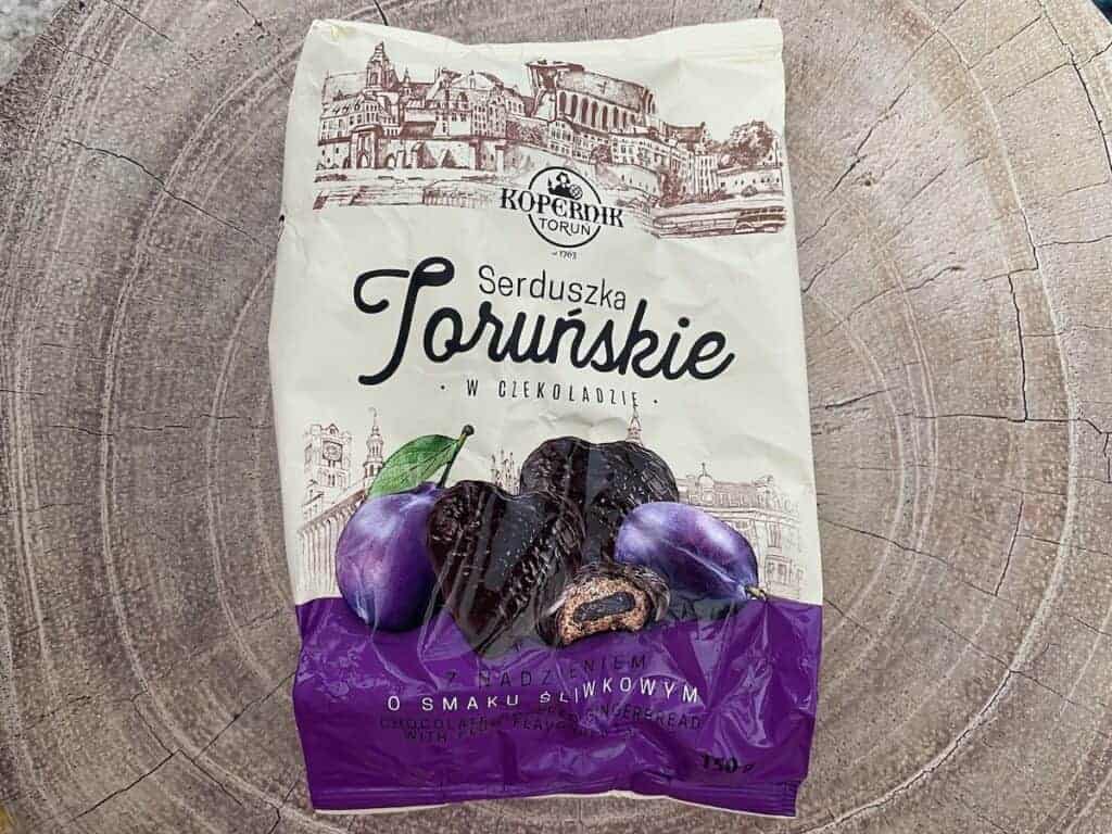 A bag of Kopernik Toruń Serduszka Toruńskie chocolate-covered plum-flavored cookies, a delicious Poland souvenir, rests on a wooden surface.