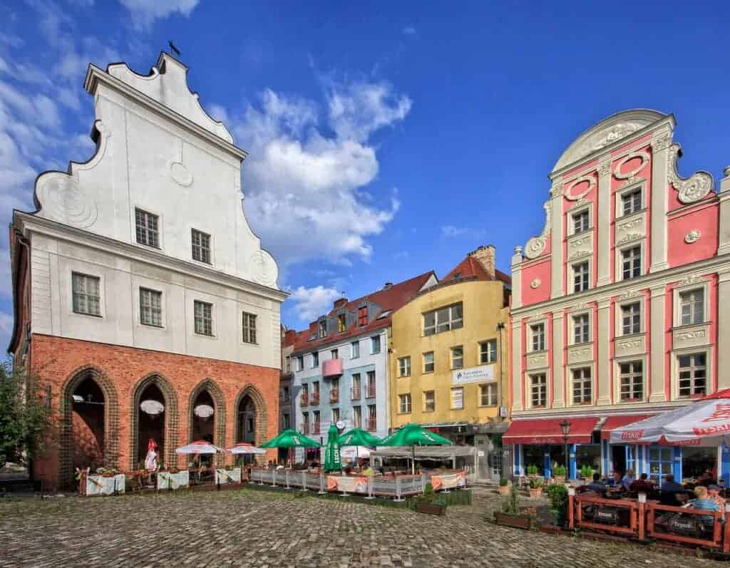 A cobblestone square with outdoor seating, featuring historic buildings with ornate facades under a blue sky—an ideal stop on your Day Trip to Poland.