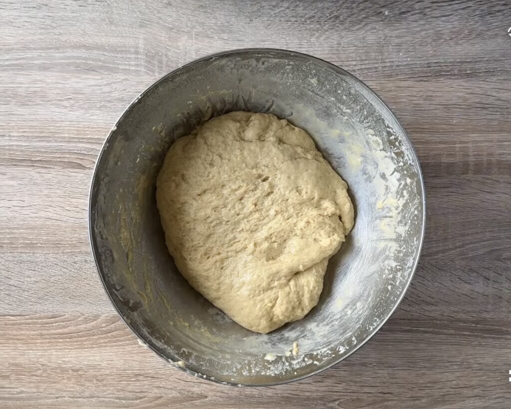 A metal bowl containing a ball of risen bread dough sits on a wooden surface, ready to be transformed into delicious Polish Apple Yeast Buns&mdash;an easy recipe for homemade drożdż&oacute;wki.