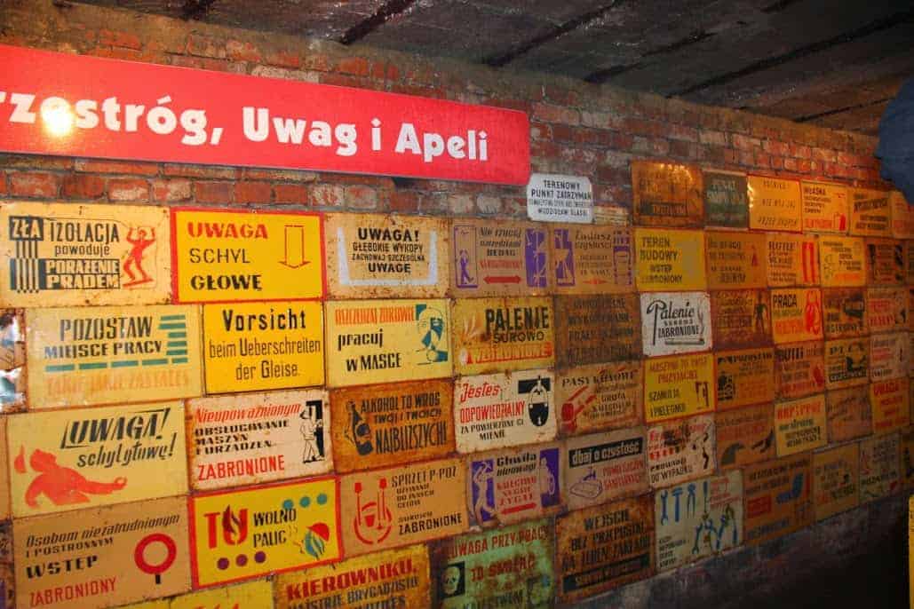 A brick wall covered with numerous vintage warning and prohibition signs in Polish and German, displayed under a red banner with white text&mdash;a unique sight for Poland travel enthusiasts exploring Dolnośląskie tourism.