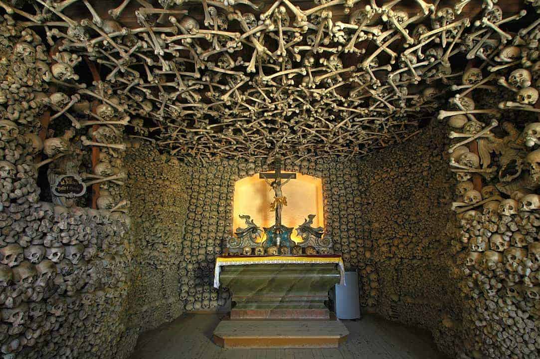 A chapel interior in Dolnośląskie, with walls and ceiling densely decorated with human skulls and bones, centered around an altar with a crucifix&mdash;one of the best places to visit for those interested in unique Poland travel experiences.