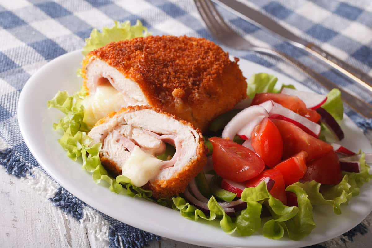 Polish chicken kiev stuffed with cheese and tomatoes on a white plate.