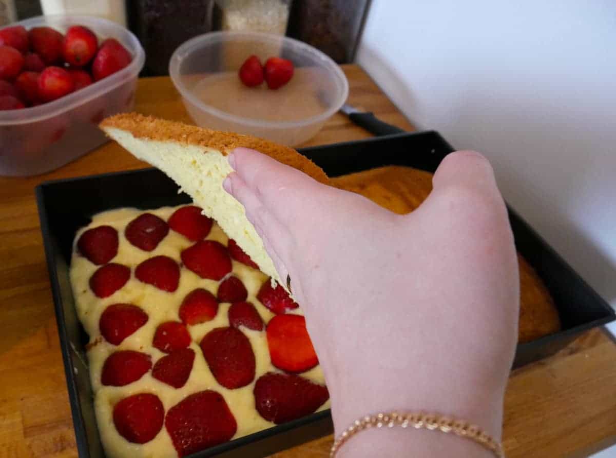 A person removing a slice of authentic Polish Tort Truskawkowy from a tray.
