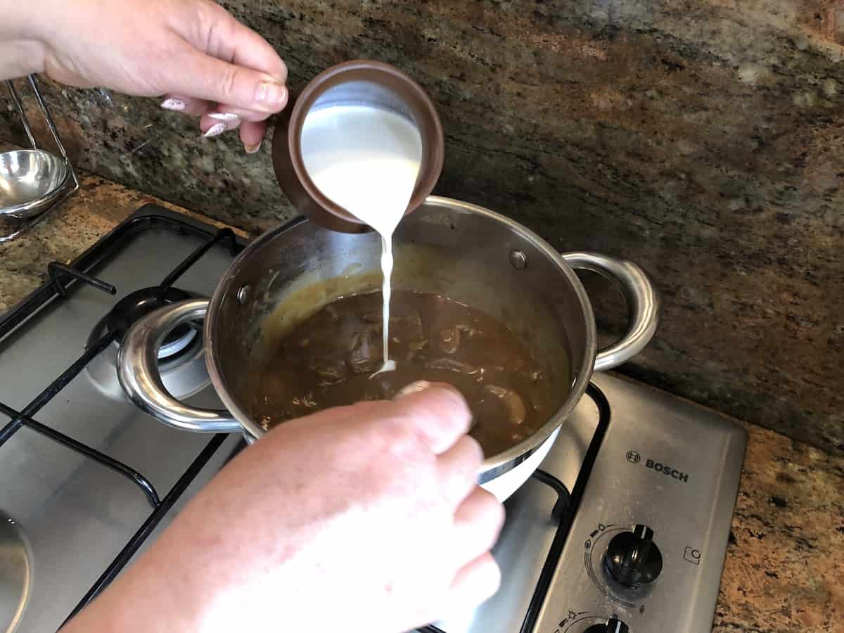 A person preparing a traditional Polish dish by pouring milk into a pot on a stove.