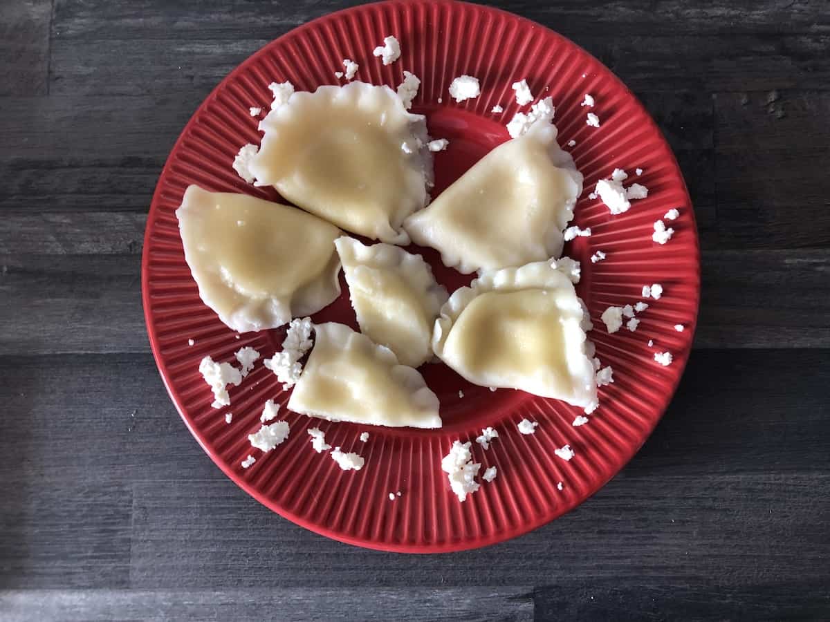 pierogi ze słodkim serem in a red plate topped with cheese crumbs.