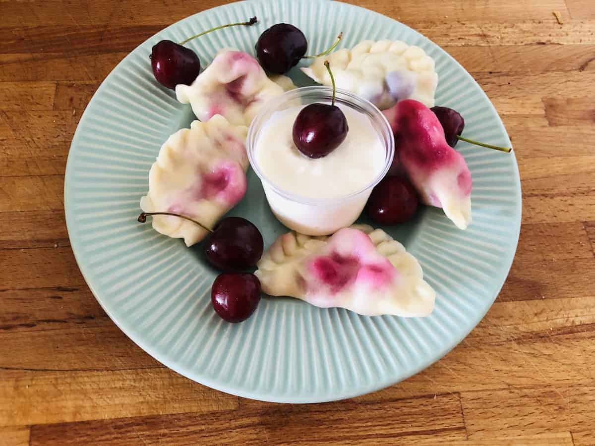 Top view of a blue plate with cherry pierogi.