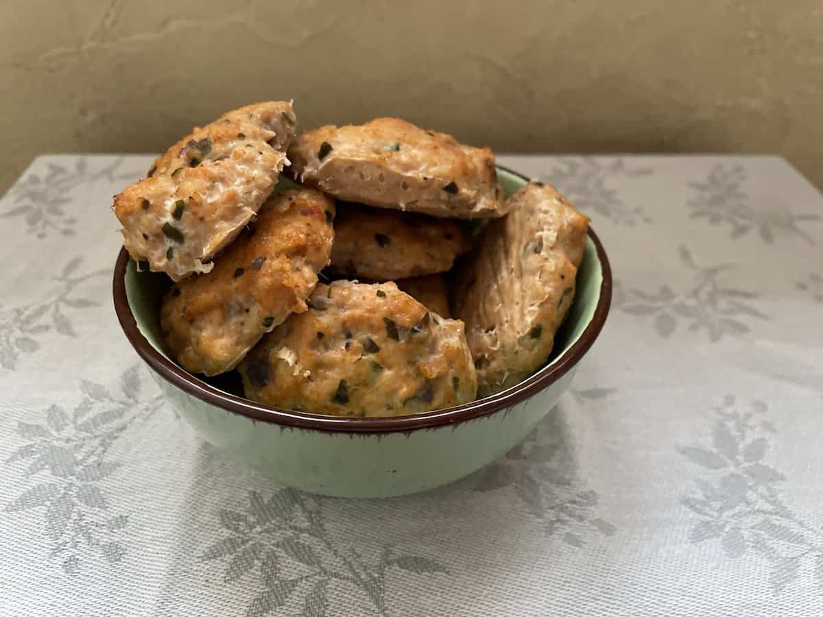 A bowl of freshly baked chicken cutlets with herbs on a tablecloth.