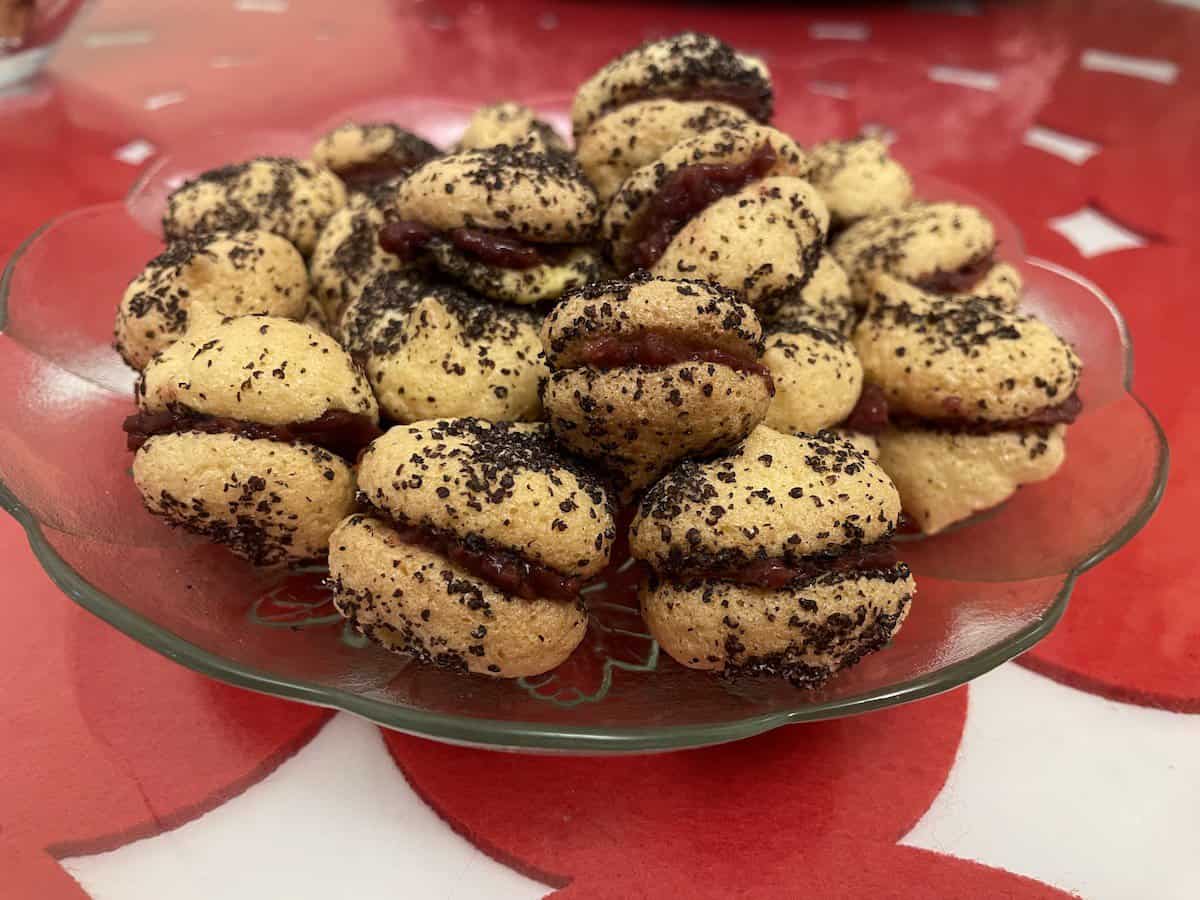 A glass bowl of Polish poppy seed cookies dusted with dark spices on a red-patterned tablecloth.