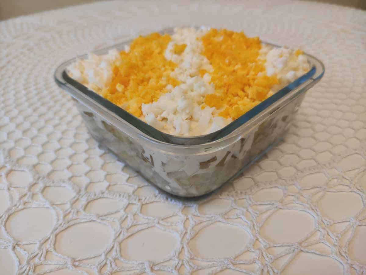 A classic Polish Herring Salad Recipe featuring a square glass dish filled with cheese and croutons.